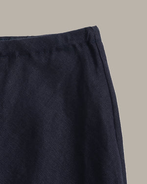 Close-up detail shot of a dark navy textured fabric garment, showing the waistband and side seam against a solid neutral beige background.