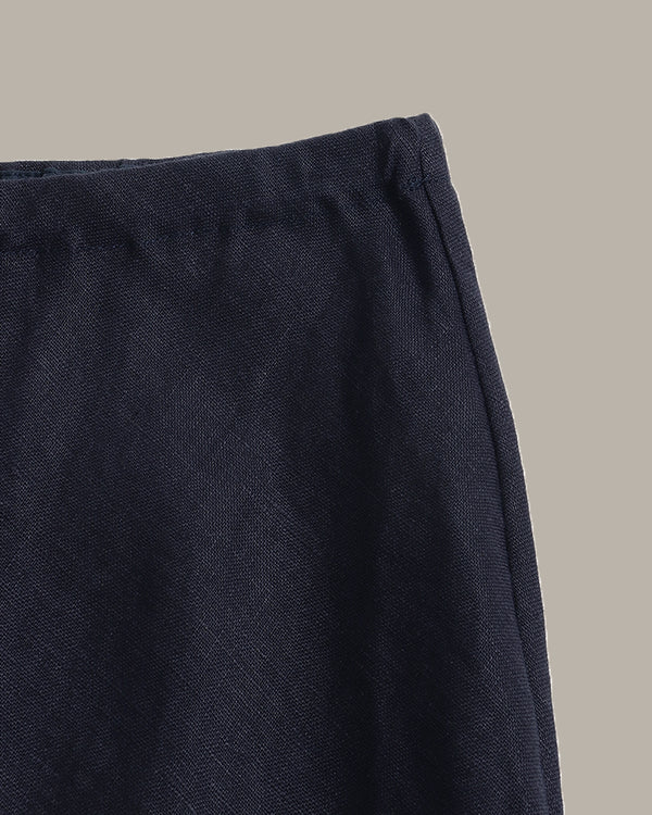 Close-up detail shot of a dark navy textured fabric garment, showing the waistband and side seam against a solid neutral beige background.