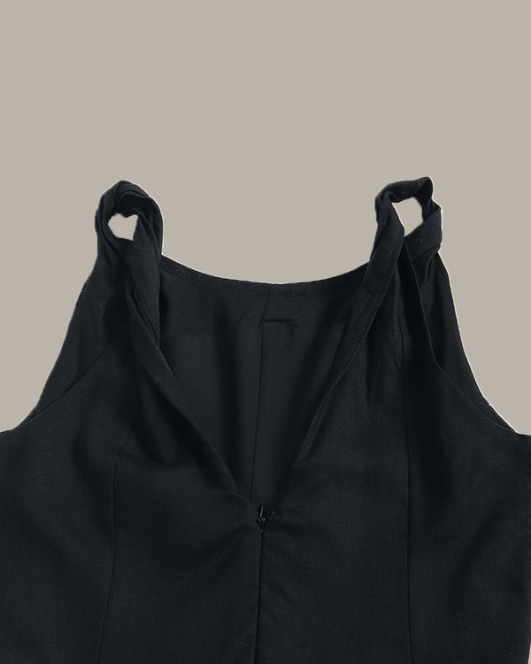 Close-up of a black sleeveless top with a deep V-neckline and gathered shoulder straps, shown against a solid taupe background.