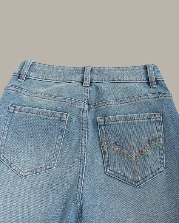 Close-up back view of light blue denim jeans showing the waistband, belt loops, and back pockets, with multicolored embroidered details on the right pocket.