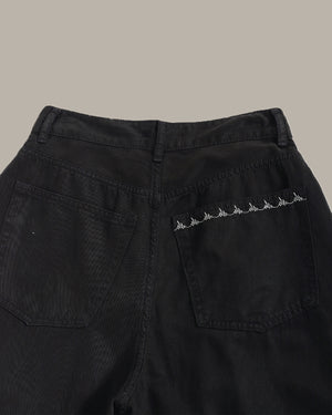 Close-up of the back waistband and right rear pocket of black denim jeans, featuring a row of white embroidered mountain motifs on the pocket.