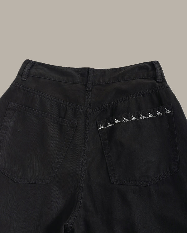 Close-up of the back waistband and right rear pocket of black denim jeans, featuring a row of white embroidered mountain motifs on the pocket.