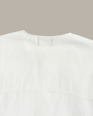 Close-up of the back neckline of a white top or dress, showing a gathered collar and seam details against a plain taupe background.