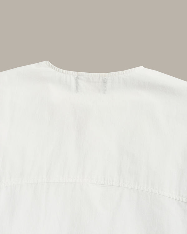 Close-up of the back neckline of a white top or dress, showing a gathered collar and seam details against a plain taupe background.
