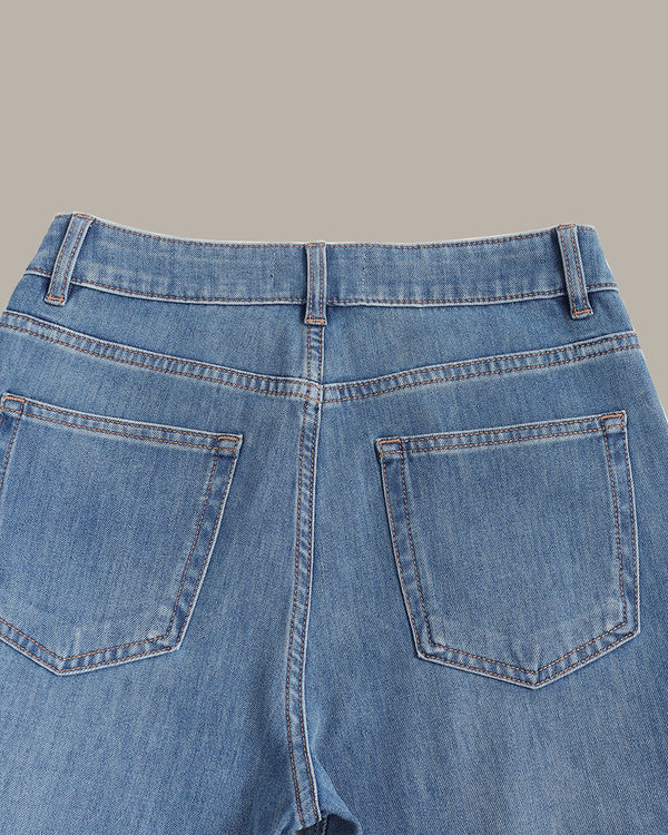 Close-up back view of light blue denim jeans showing the waistband, belt loops, and back pockets against a solid beige background.