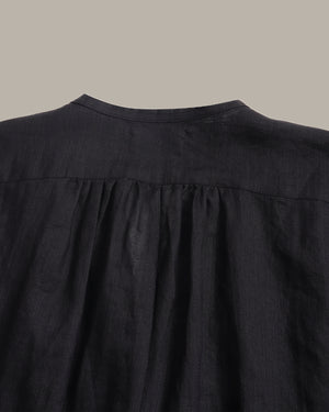 Close-up of the back of a black linen blouse with a gathered, pleated neckline, set against a solid taupe background.