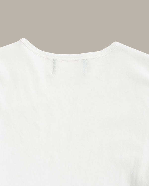 Close-up of the back neckline of a plain white short-sleeve top against a solid taupe background.