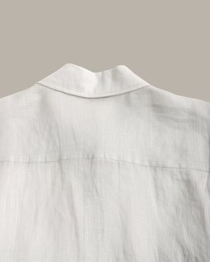Close-up of a white linen shirt showing the collar and back fabric texture against a solid taupe background.