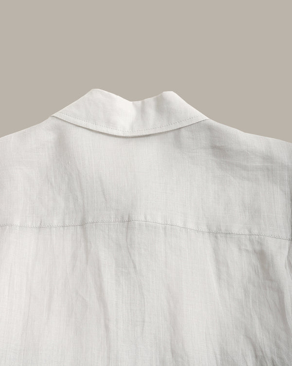 Close-up of a white linen shirt showing the collar and back fabric texture against a solid taupe background.