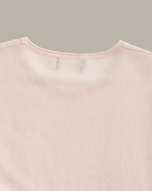 Close-up of a light pink ribbed knit garment, showing the inner neckline with two small stitched brand tags on a solid taupe background.