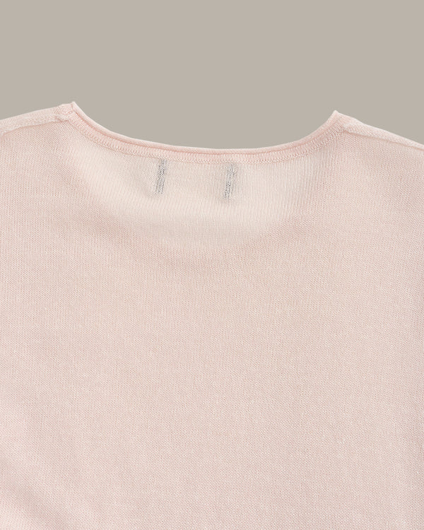 Close-up of a light pink ribbed knit garment, showing the inner neckline with two small stitched brand tags on a solid taupe background.