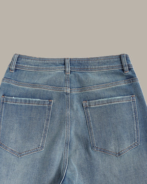 Close-up back view of light blue denim jeans showing the waistband, belt loops, and back pockets against a solid taupe background.