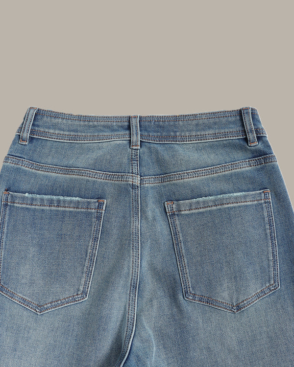 Close-up back view of light blue denim jeans showing the waistband, belt loops, and back pockets against a solid taupe background.