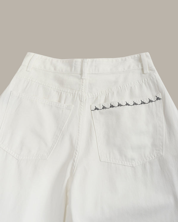 Close-up of the back waistband and right back pocket of white denim jeans, featuring a row of small black embroidered bird motifs along the pocket edge.