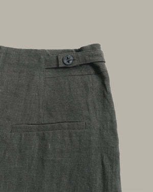 Close-up of the waistband and back pocket of dark gray textured trousers, showing a button closure and fabric weave against a solid taupe background.