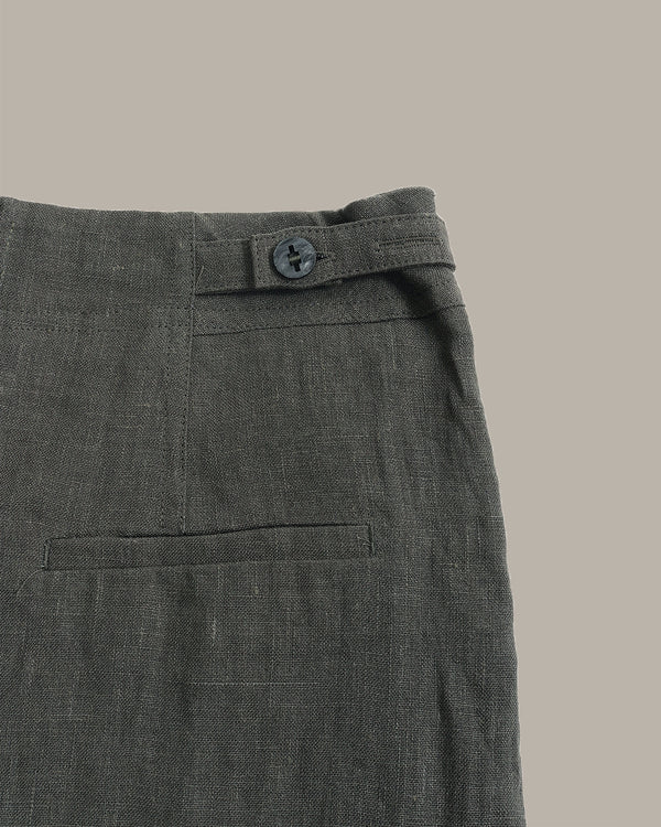 Close-up of the waistband and back pocket of dark gray textured trousers, showing a button closure and fabric weave against a solid taupe background.