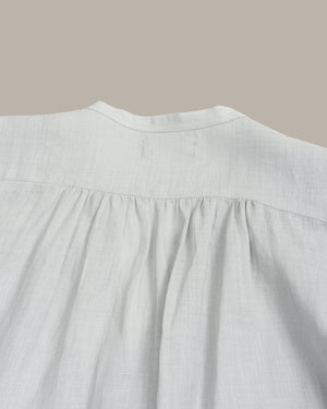 Close-up of a light gray linen blouse showing the back neckline with a gathered, pleated design.