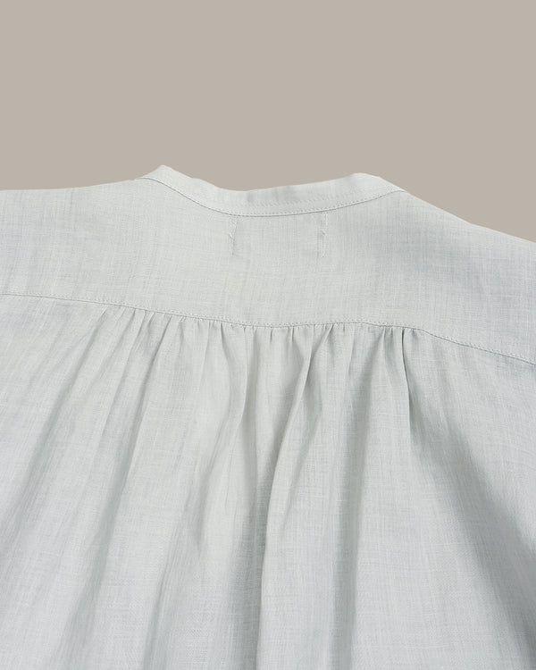 Close-up of a light gray linen blouse showing the back neckline with a gathered, pleated design.