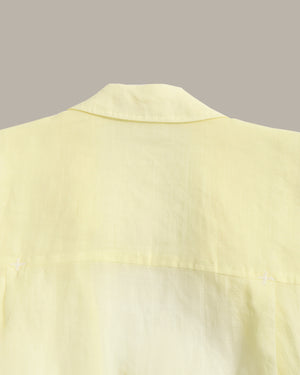 Close-up of a pale yellow shirt showing the collar and upper chest fabric against a solid taupe background.