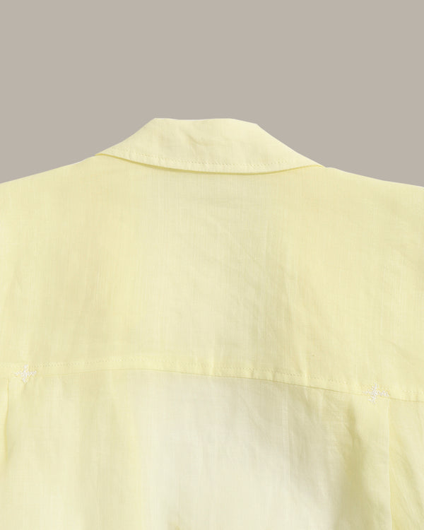 Close-up of a pale yellow shirt showing the collar and upper chest fabric against a solid taupe background.