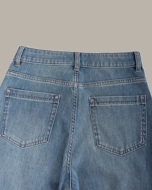 Close-up back view of blue denim jeans showing the waistband, belt loops, and back pockets on a solid beige background.