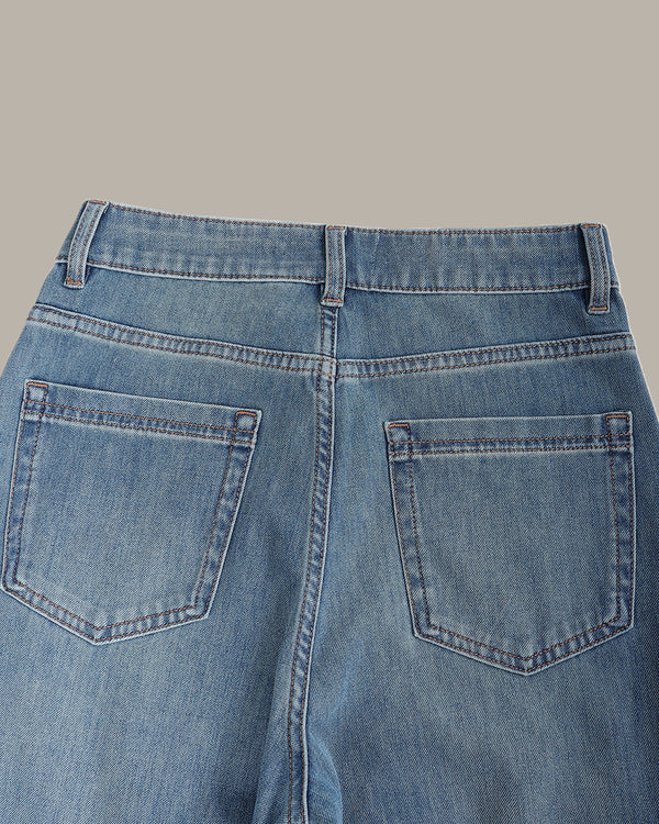 Close-up back view of blue denim jeans showing the waistband, belt loops, and back pockets on a solid beige background.
