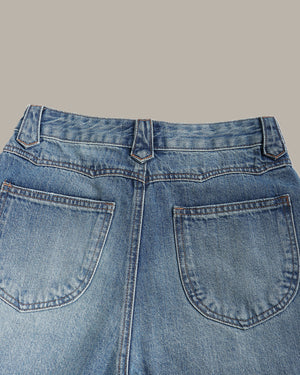 Close-up of the back waistband and pockets of light blue denim jeans against a solid beige background.