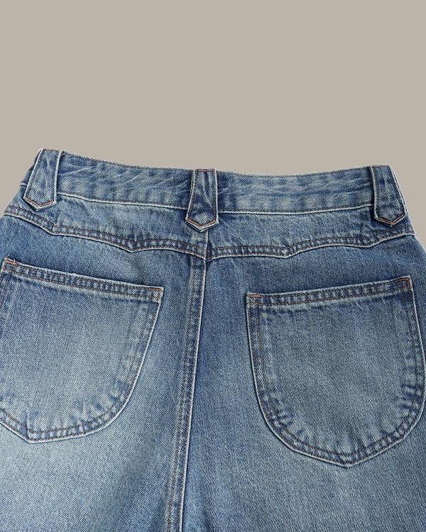 Close-up of the back waistband and pockets of light blue denim jeans against a solid beige background.
