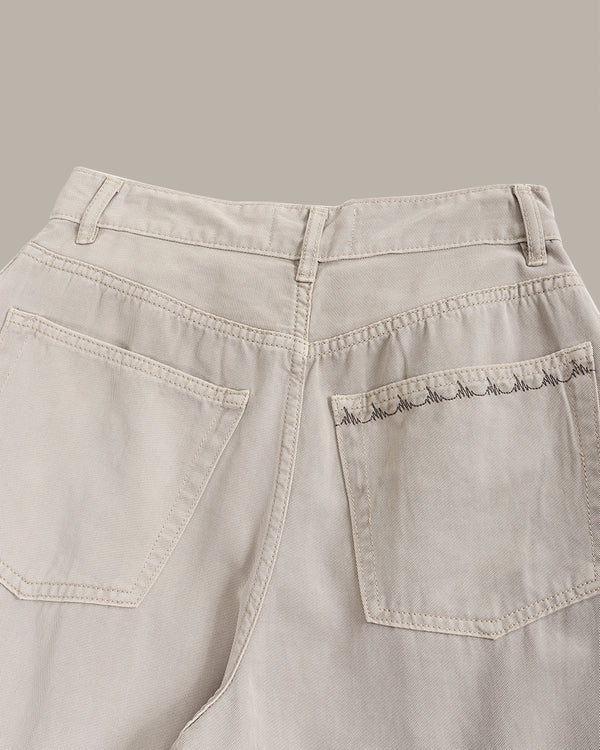 Close-up of the back waistband and rear pockets of light beige denim jeans, showing a decorative scalloped embroidery on the right pocket.