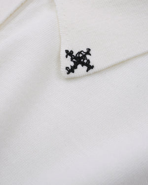 Close-up of a white knit fabric with a small black embroidered monogram logo on the collar.