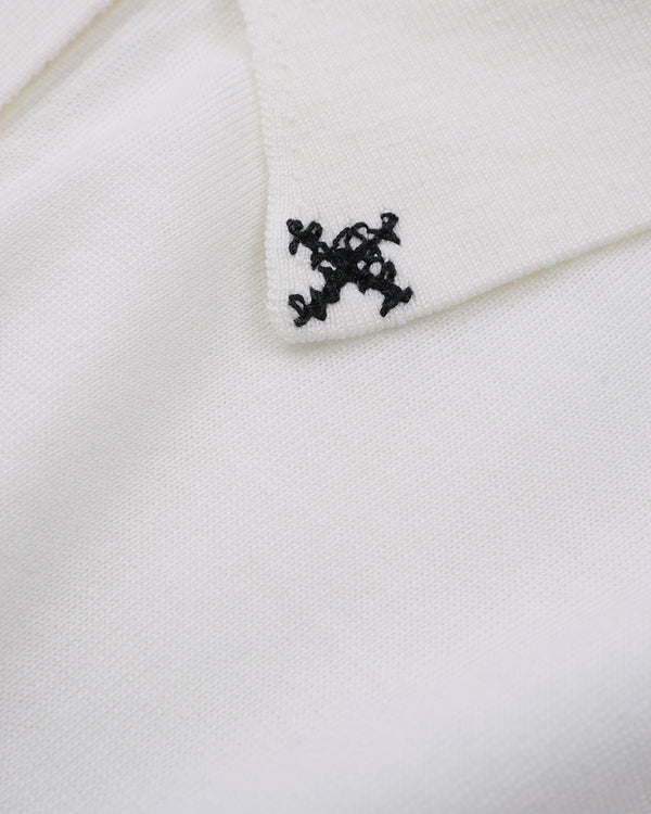 Close-up of a white knit fabric with a small black embroidered monogram logo on the collar.