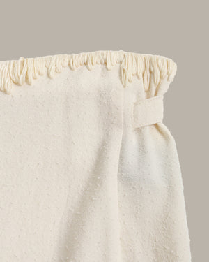Close-up of a textured white skirt with a subtle stitch pattern on a beige background