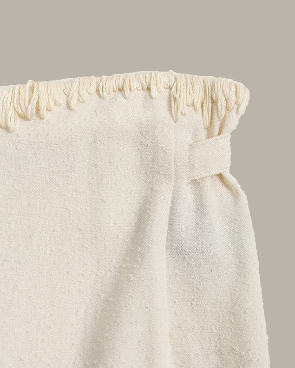 Close-up of a textured white skirt with a subtle stitch pattern on a beige background