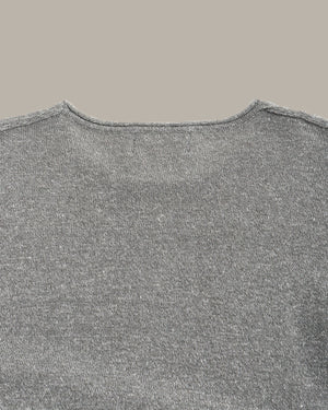 Close-up of a gray knit sweater showing the back neckline and textured fabric against a solid taupe background.