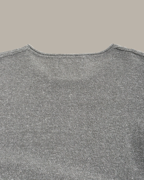 Close-up of a gray knit sweater showing the back neckline and textured fabric against a solid taupe background.