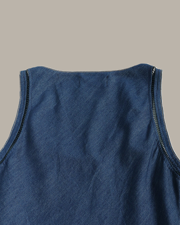 Close-up of the back neckline of a sleeveless blue top, showing dark contrast stitching along the armholes and a zipper at the shoulder, on a solid taupe background.