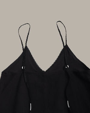 Black spaghetti-strap camisole top with delicate lace trim along the V-neckline, shown against a solid taupe background.