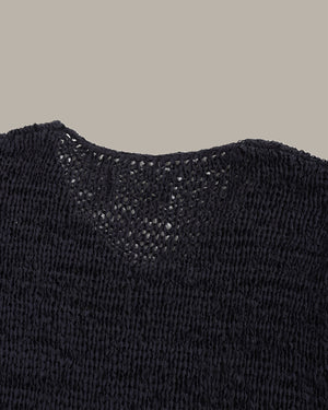 Close-up of a black knit sweater showing the textured knit pattern and a V-neck opening against a solid taupe background.