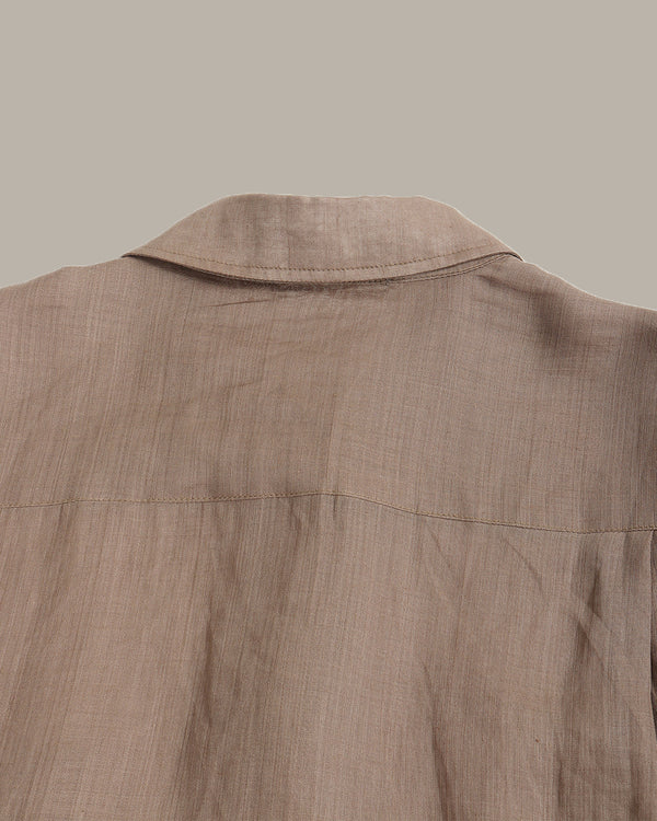 Close-up of the back collar and upper back of a light brown linen shirt, showing the textured fabric and stitching against a solid taupe background.