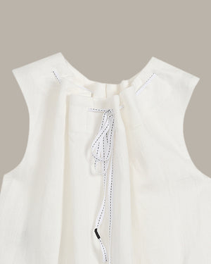 Close-up of a white sleeveless top with a subtle pattern on a beige background