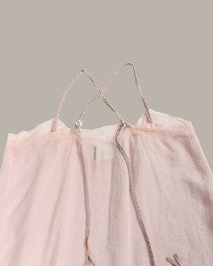 A pale blush pink sheer mesh camisole top with braided rope straps and delicate lace trim, shown against a solid taupe background.