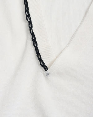 Close-up of a white knit garment with a black braided trim detail along the neckline.