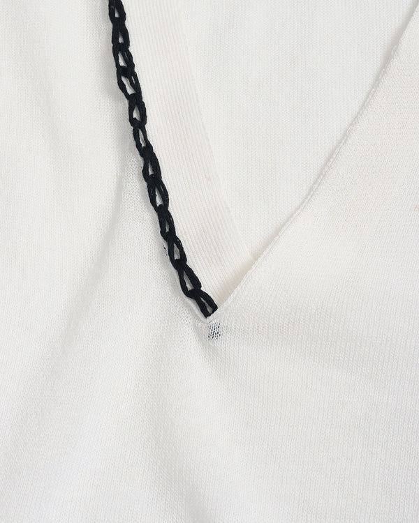 Close-up of a white knit garment with a black braided trim detail along the neckline.