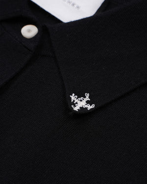 Close-up of a black knit polo shirt collar with a small white embroidered logo and a white button.