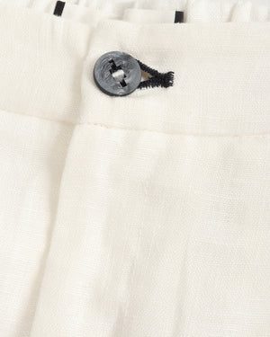 Close-up of off-white textured fabric with a dark gray button and black thread detail at the waistband.