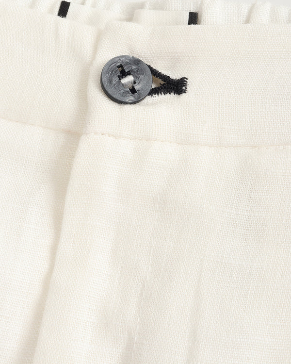 Close-up of off-white textured fabric with a dark gray button and black thread detail at the waistband.
