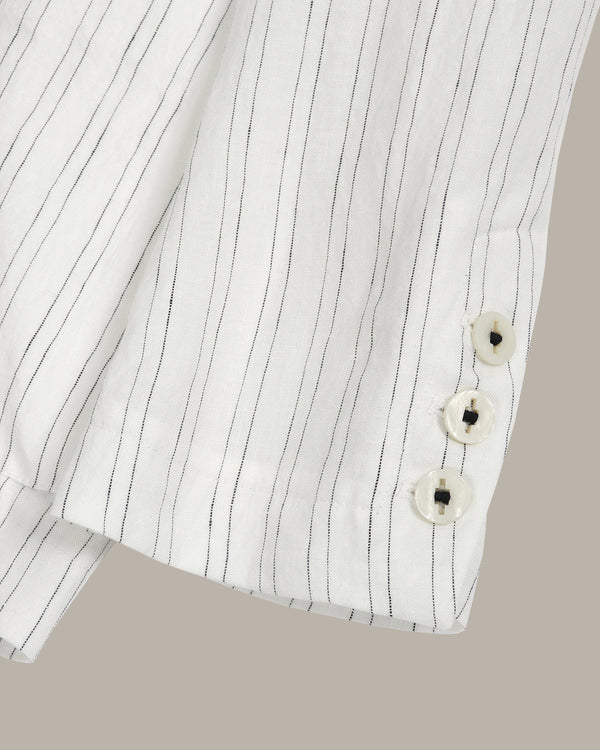 Close-up of a white shirt with black pinstripes and floral buttons on a beige background