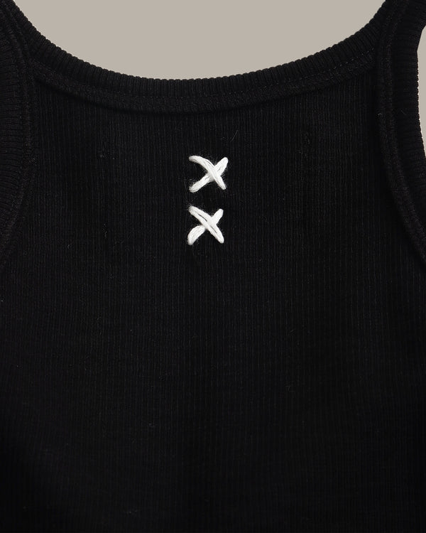 Black tank top with white embroidered design on a beige background