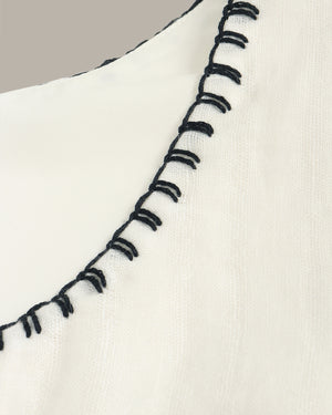 Close-up of a white fabric with black embroidered stitching on a neutral background