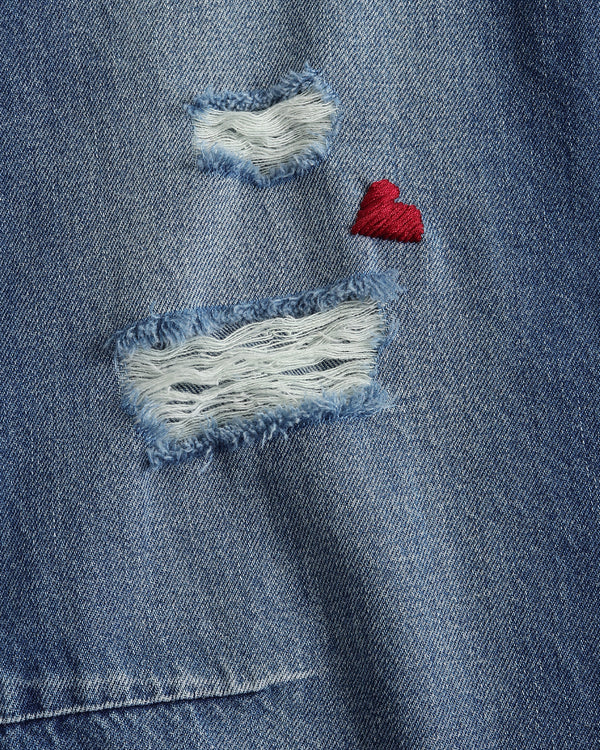 Close-up of a blue denim jacket with patches and a red heart.